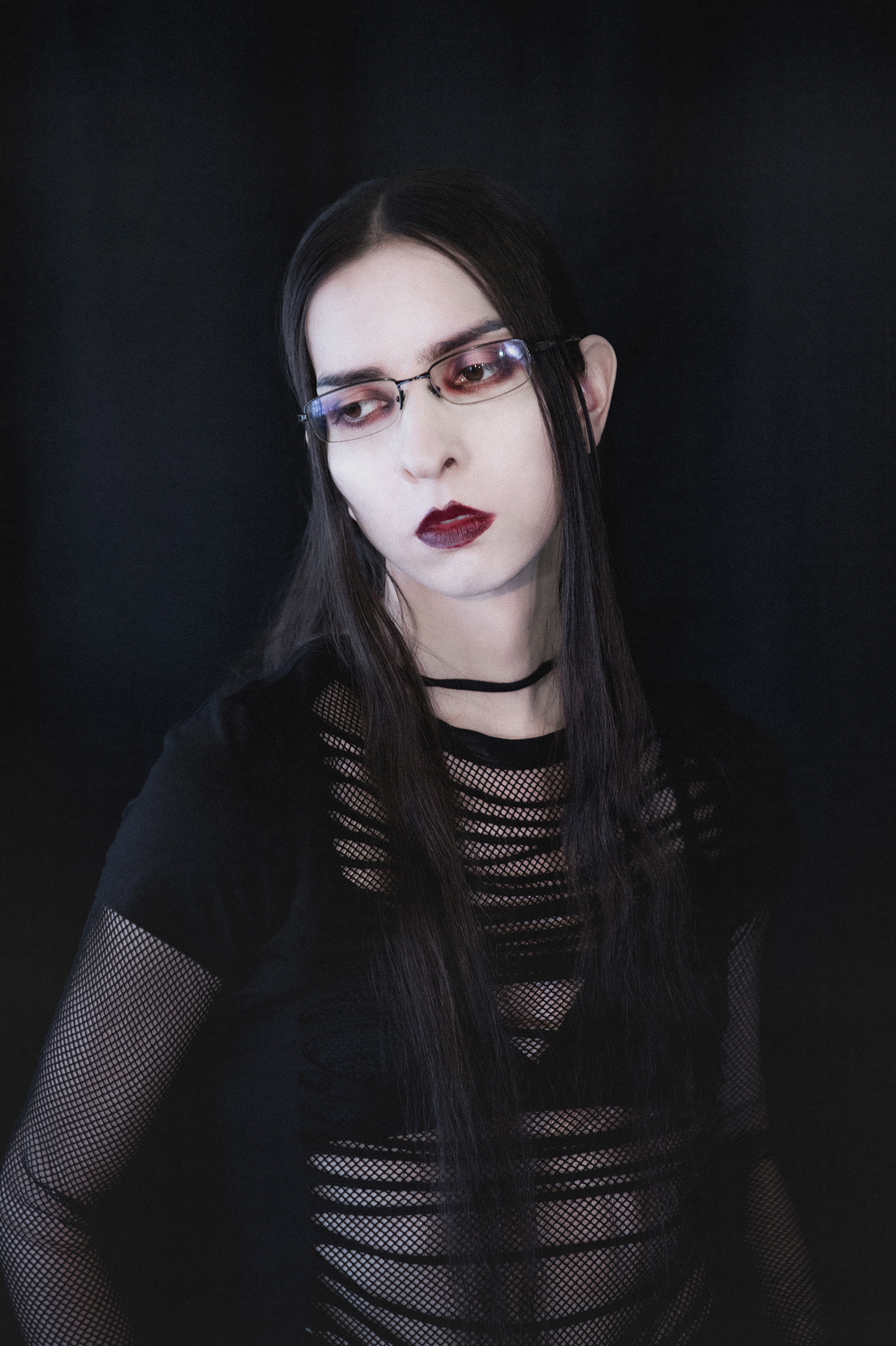 Portrait of a female model with pale skin and bruise colored eye and lip makeup against a dark backdrop